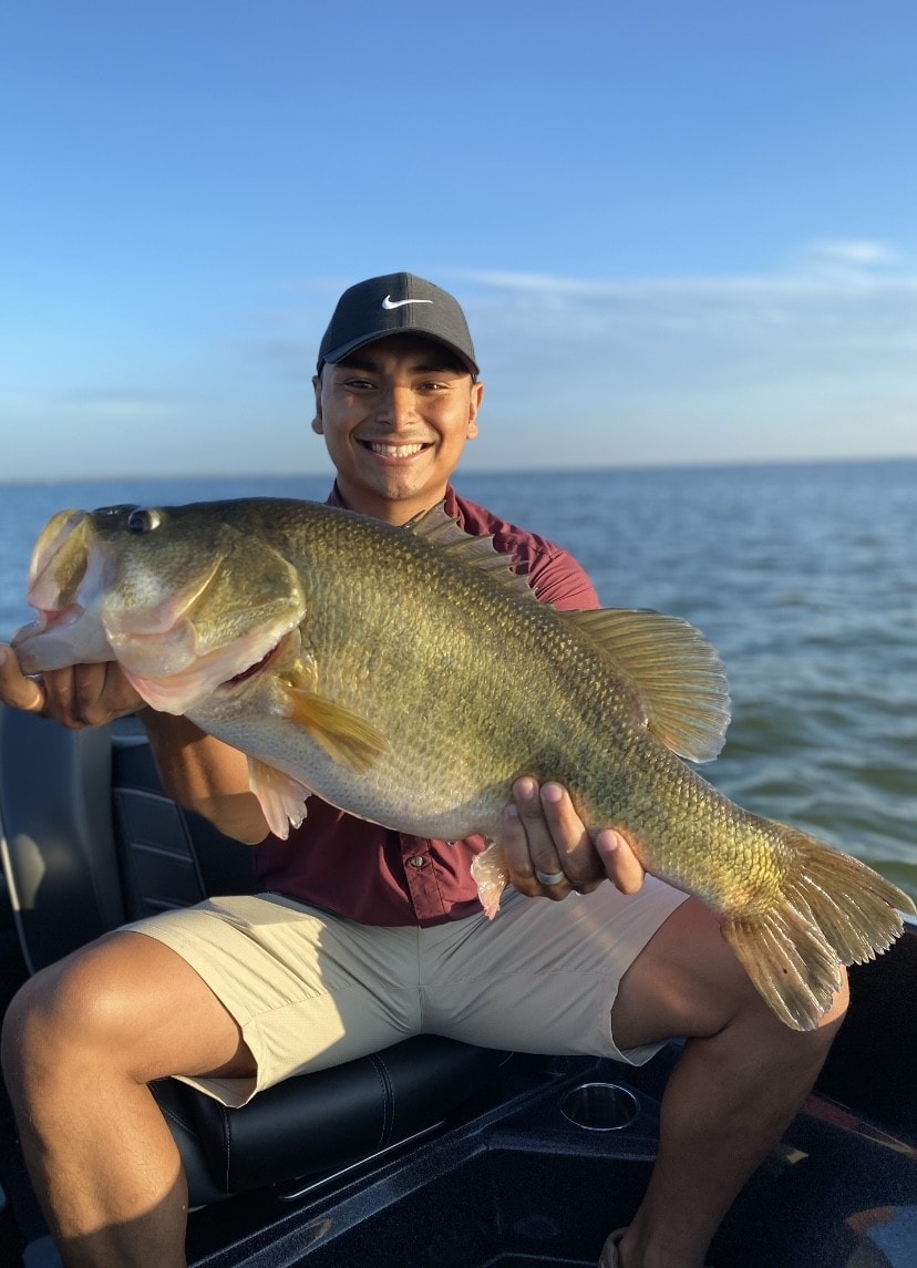 Young man in Nike cap holding giant bass at golden hour on Lake Falcon