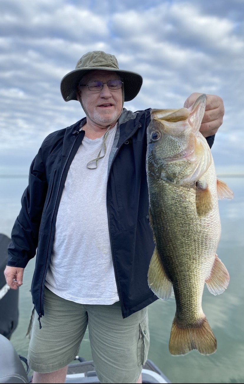 Man in bucket hat and black jacket holding bass on cloudy day