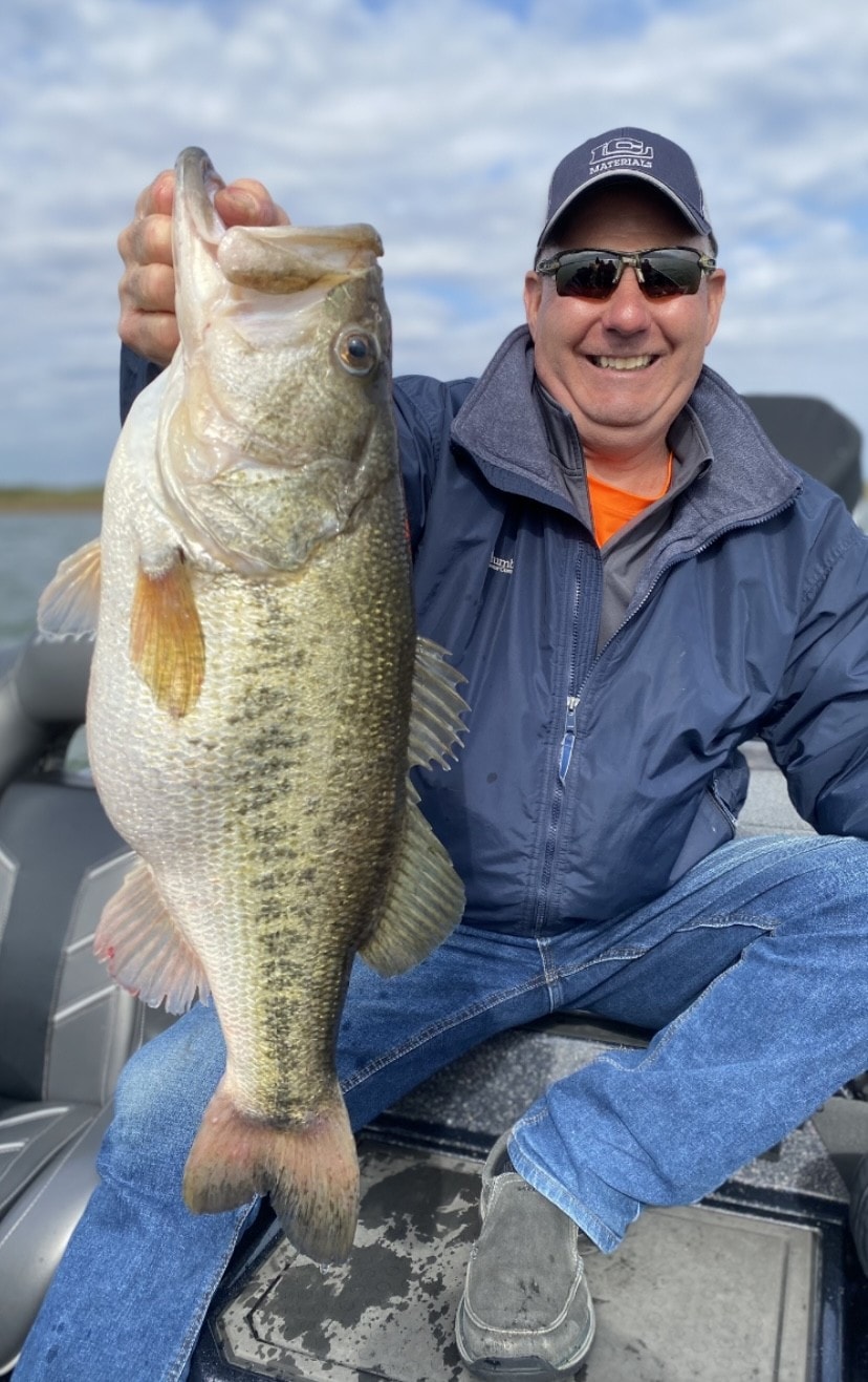 Man in LCI Materials cap holding trophy bass on cloudy day