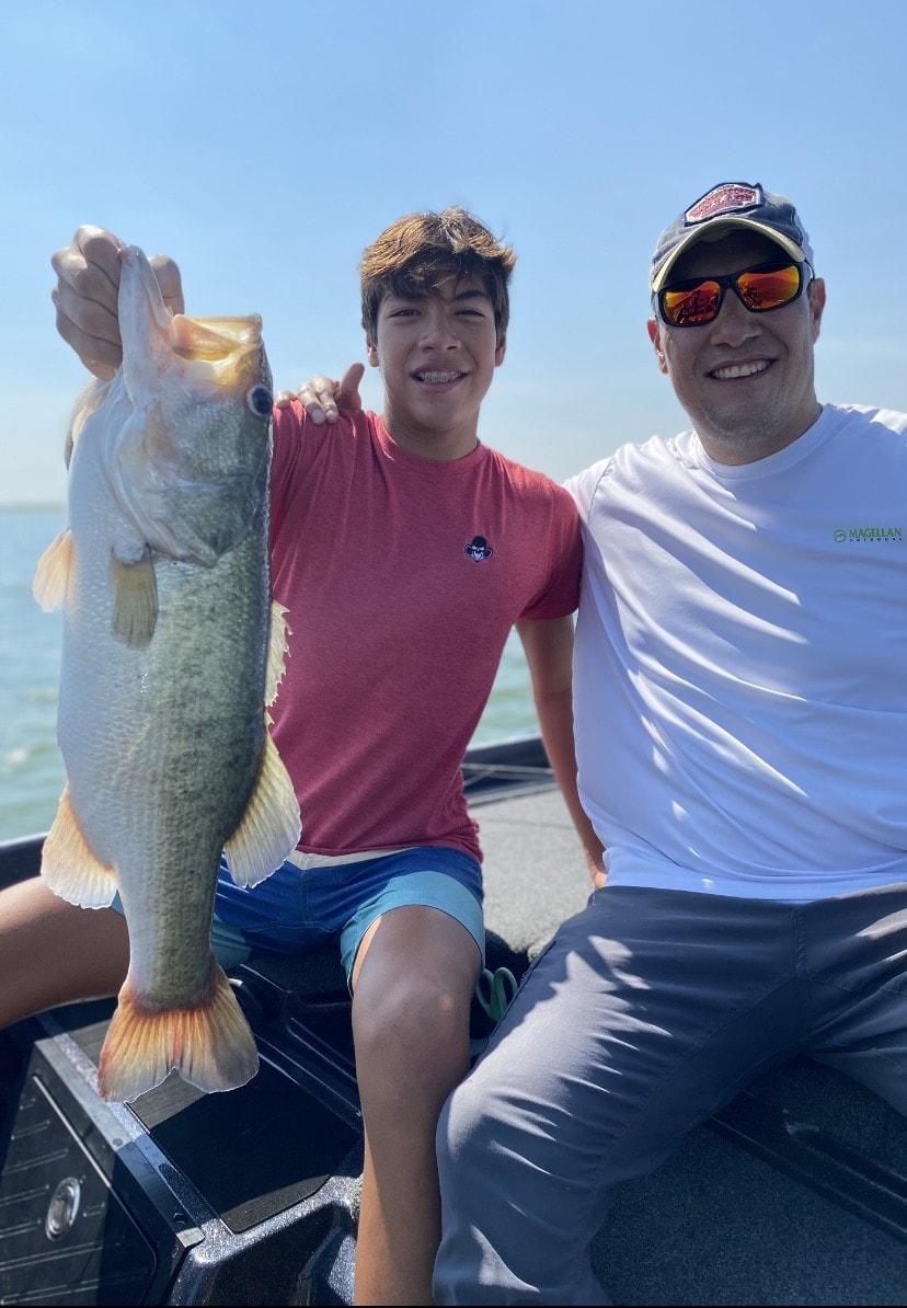 Teen and dad in Magellan shirt holding big bass on sunny day
