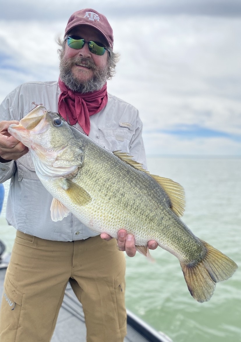 Man in A&M cap and red gaiter holding giant bass on cloudy day
