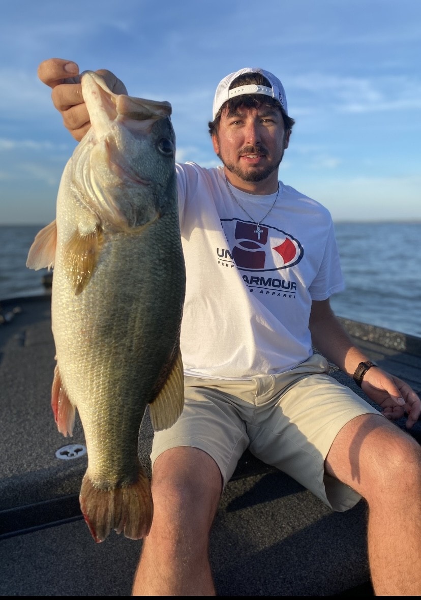 Man in Under Armour shirt holding big bass at golden hour on Lake Falcon
