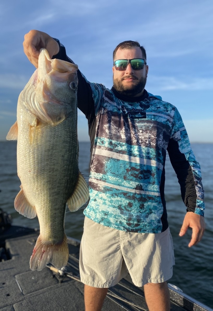 Man in camo fishing shirt holding giant bass at golden hour