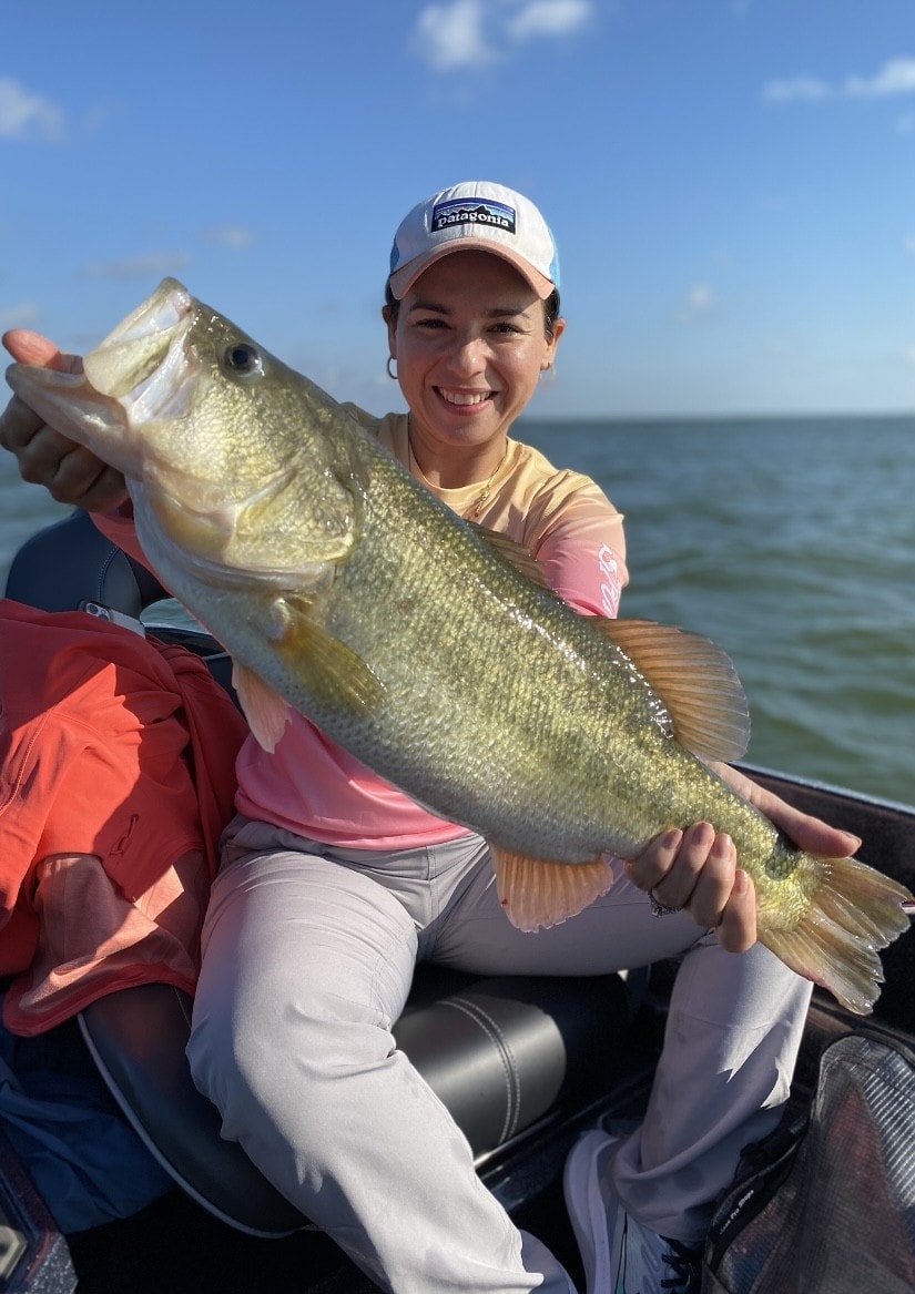 Woman in Patagonia cap holding massive bass on sunny day on Lake Falcon