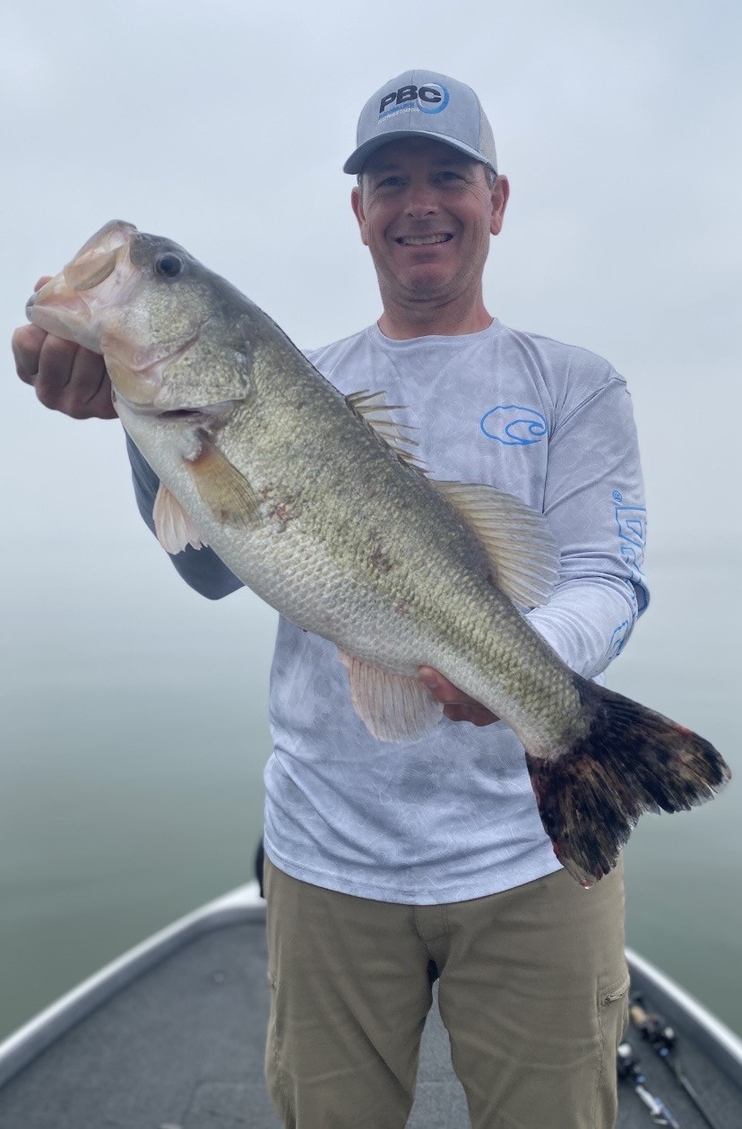 Angler in PBC cap holding trophy bass in fog
