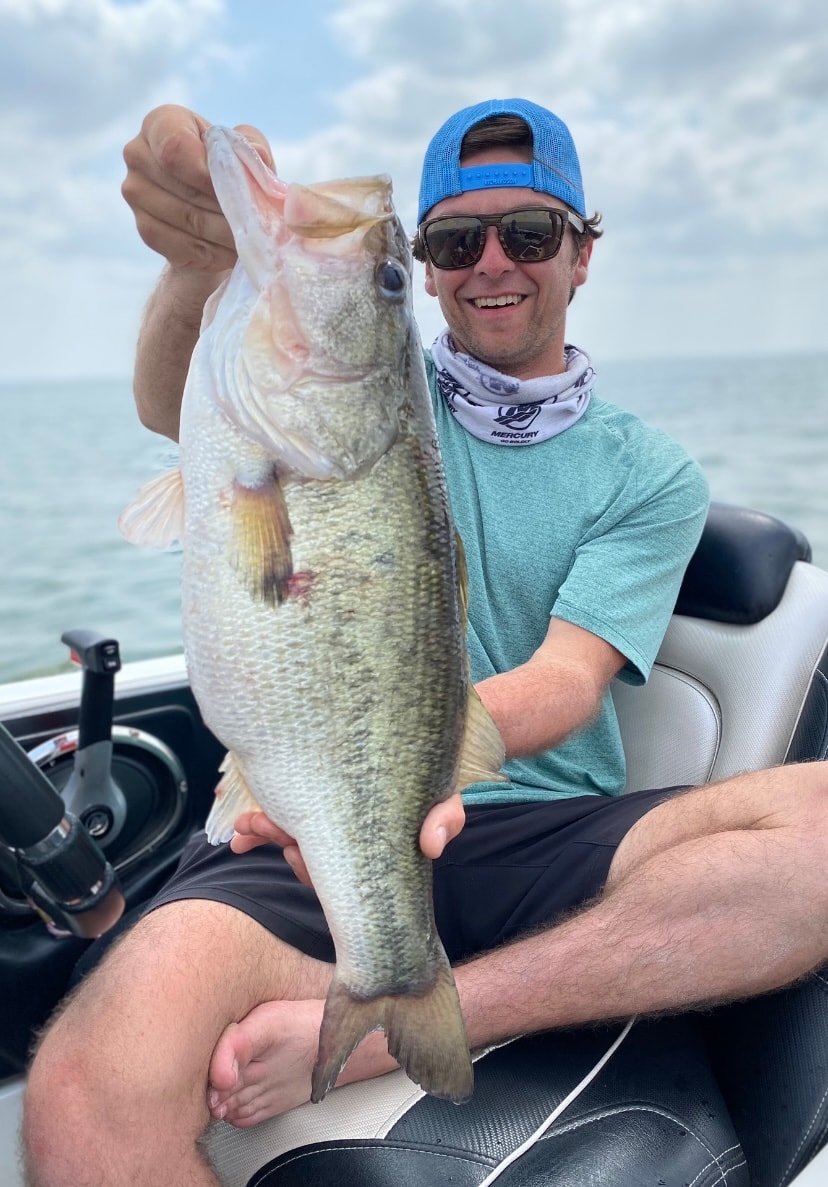 Young man in blue trucker cap holding massive bass on cloudy day