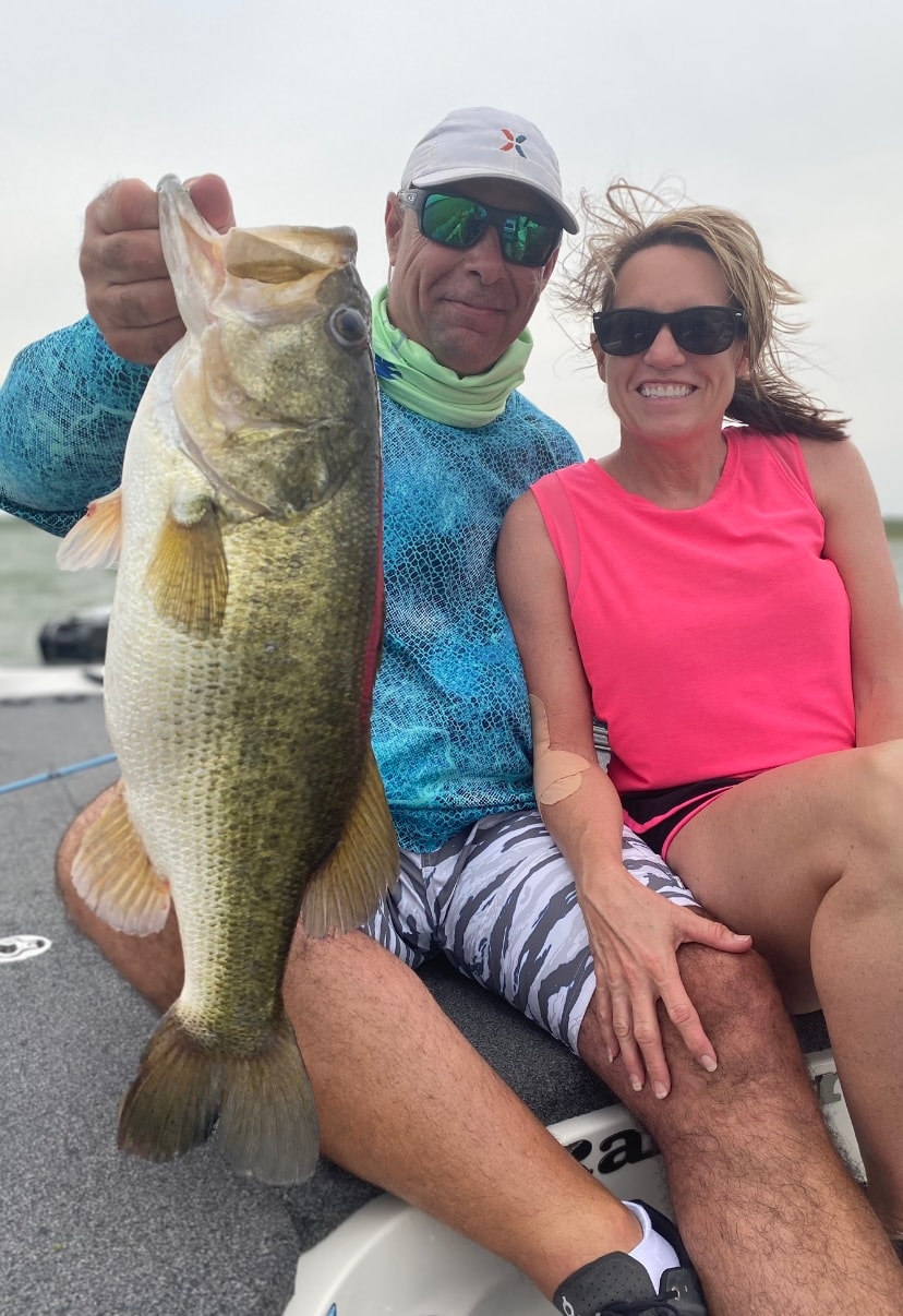Man and woman on boat with man holding giant bass on windy day