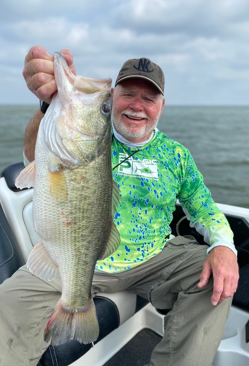 Man in NK cap and Pelagic shirt holding massive bass on cloudy day