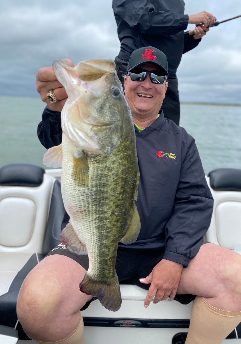 Man in Big Bite Baits cap holding massive bass on cloudy day