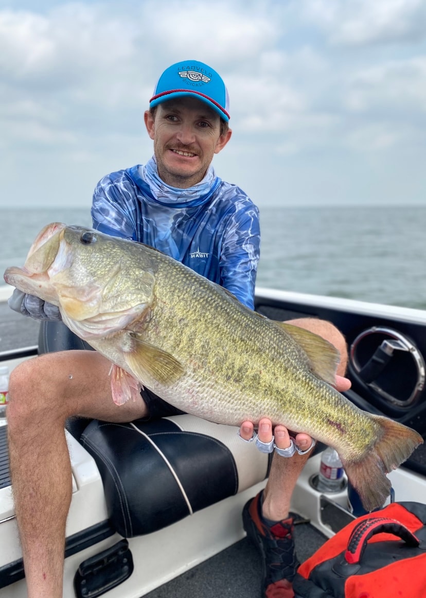 Man in Leadveld Podcast cap and Habit shirt holding giant bass on cloudy day