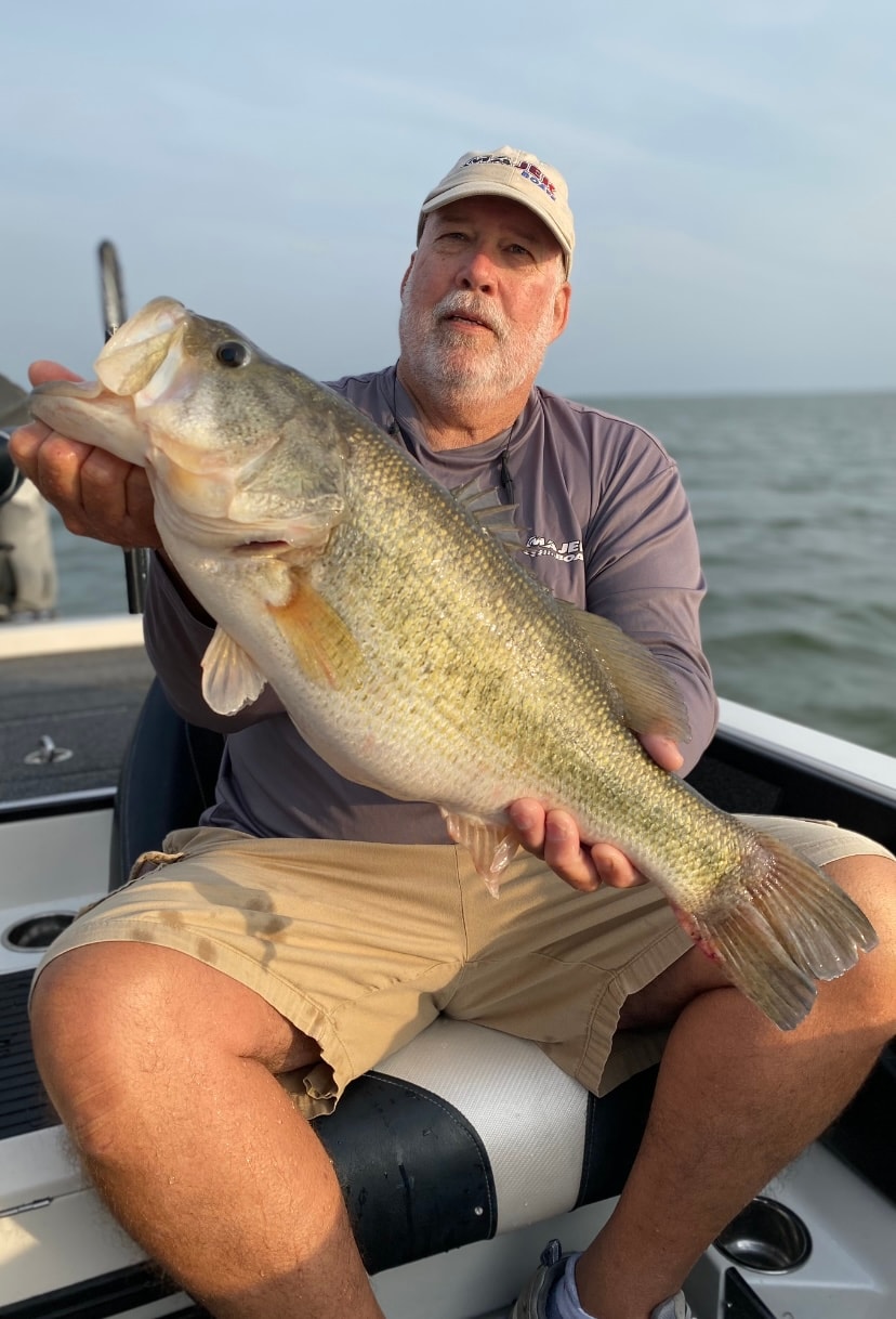 Man in Majestic Boats cap holding big bass on sunny day on Lake Falcon