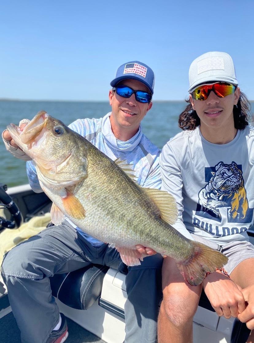 Man in American flag cap and teen in Bulldogs shirt with trophy bass on sunny day