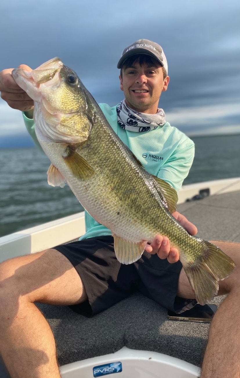 Man in Star Truck Parts cap and Magellan shirt holding big bass on cloudy day