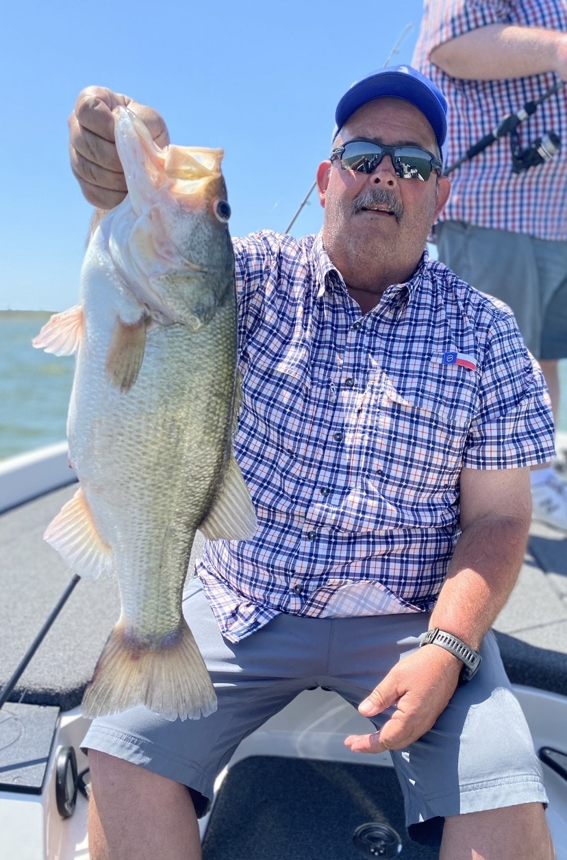 Man in blue cap and plaid shirt holding bass by the lip on sunny day