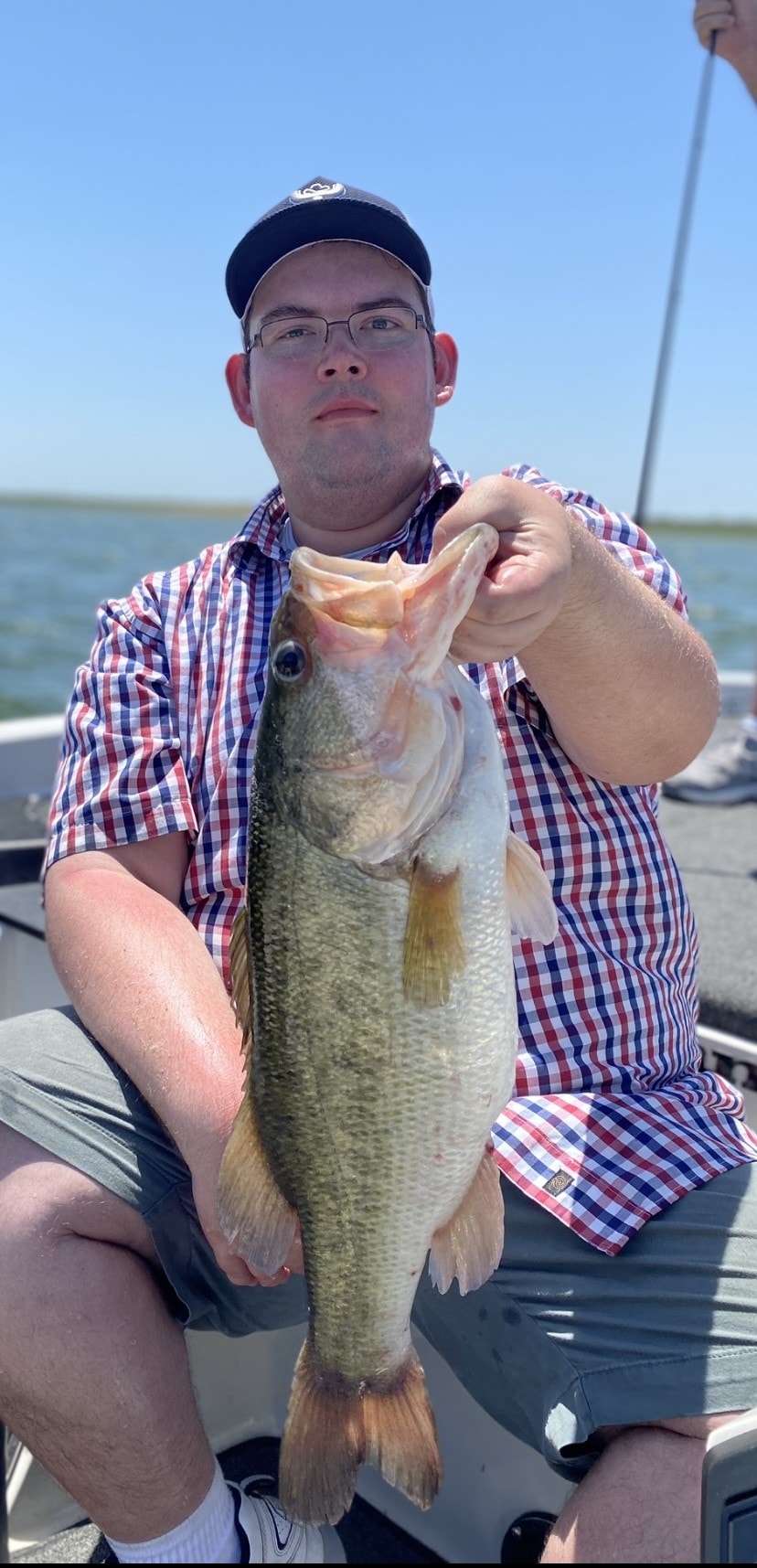 Man in plaid shirt and dark cap holding bass on sunny day on Lake Falcon