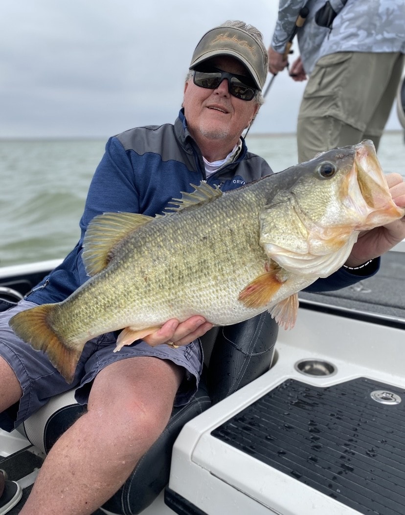 Older man in Orvis jacket holding massive bass on cloudy day on Lake Falcon