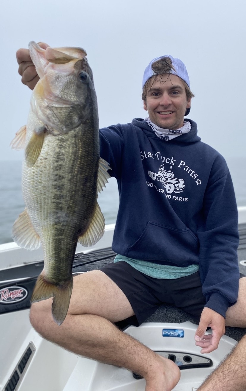 Young man in Star Truck Parts hoodie holding bass on foggy day on Ranger boat