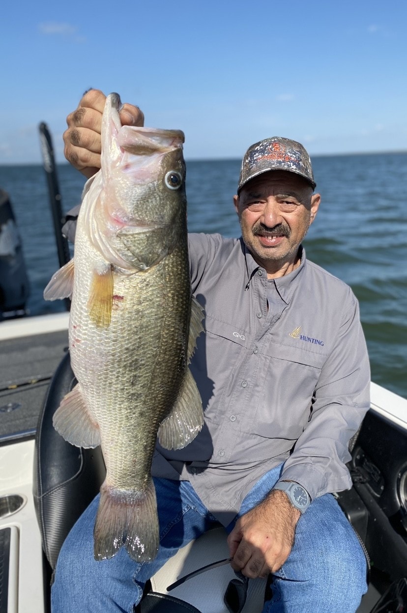 Man in gray shirt holding large bass on boat