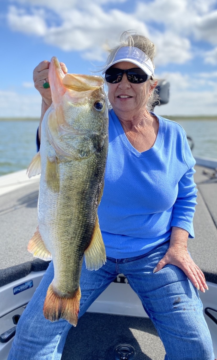 Woman in blue shirt holding large bass on boat