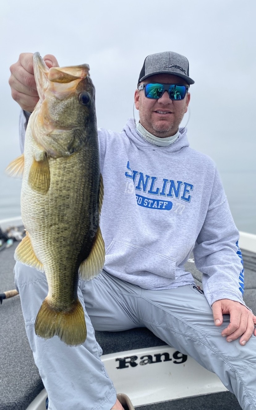 Man in gray shirt holding bass on boat
