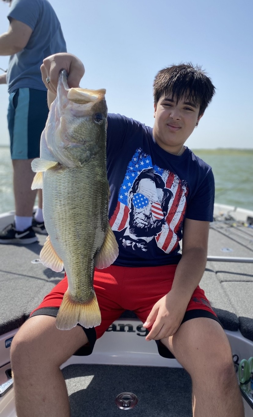 Man in white hoodie holding large bass on cloudy day