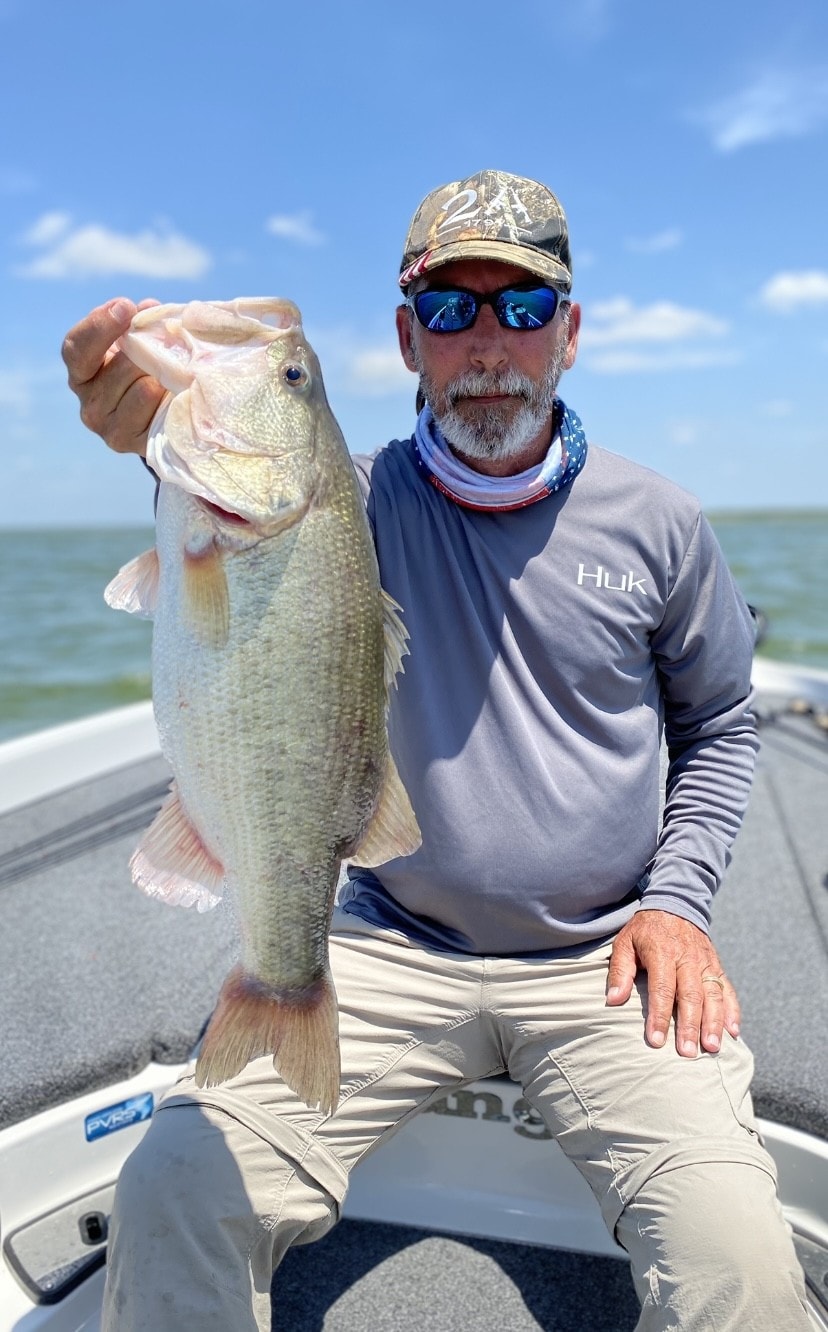 Young man in white shirt holding big bass on cloudy day