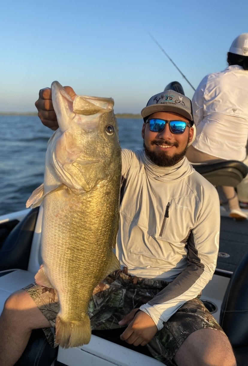 Man in Huk shirt holding large bass on sunny day