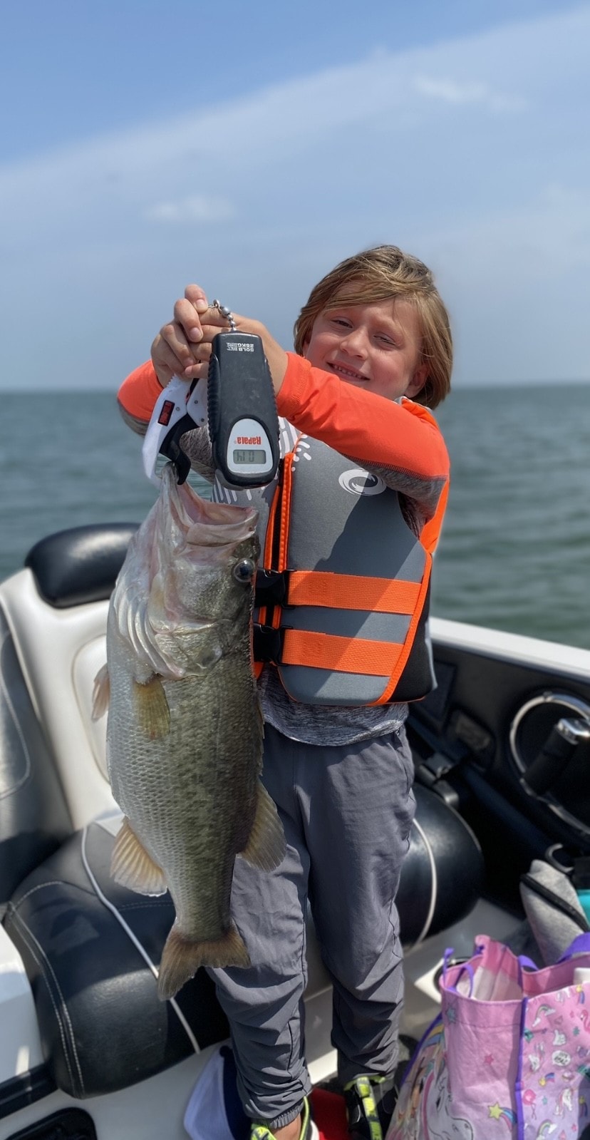 Kid in orange life vest holding large bass on boat
