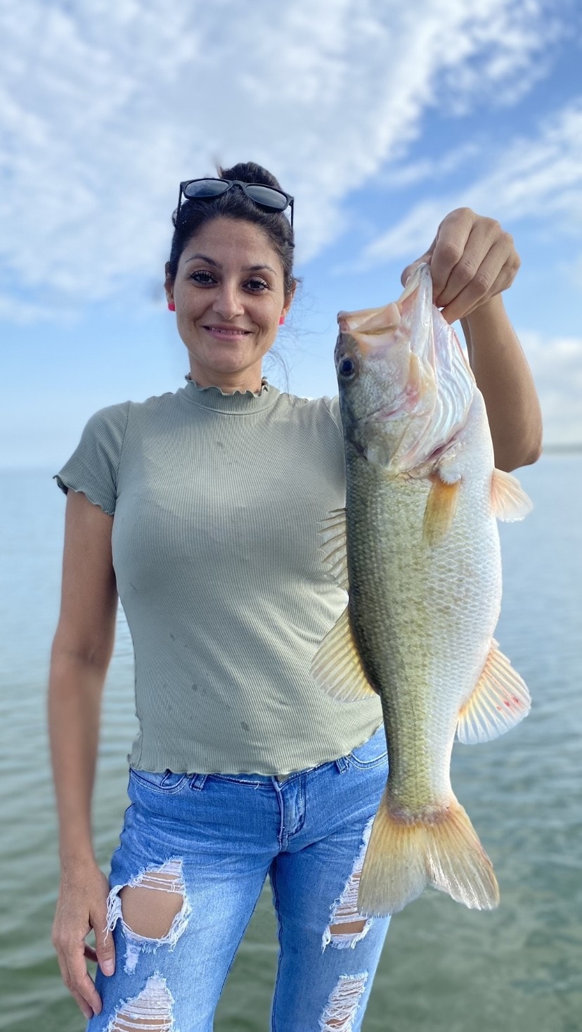 Woman in green shirt holding bass by the water