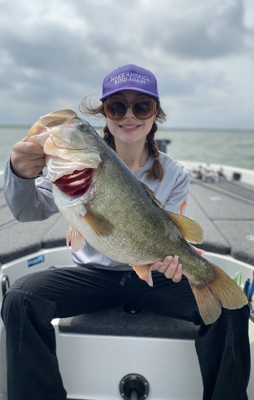 Young woman in purple cap holding massive bass on boat