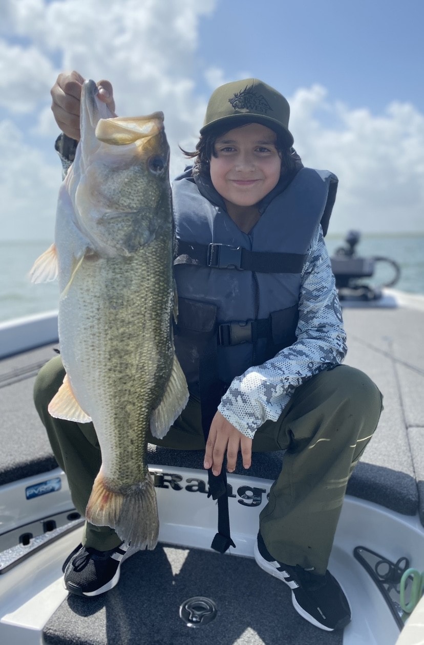Boy in camo life vest holding large bass on boat