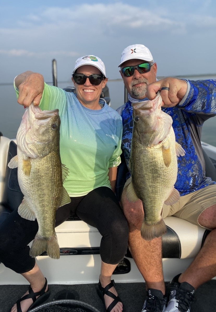 Man and woman each holding large bass on boat