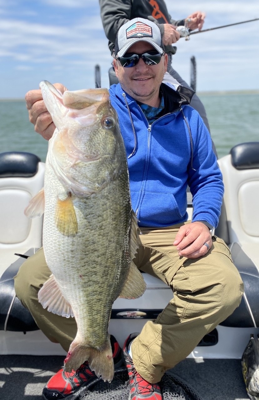 Man in blue hoodie holding large bass on boat