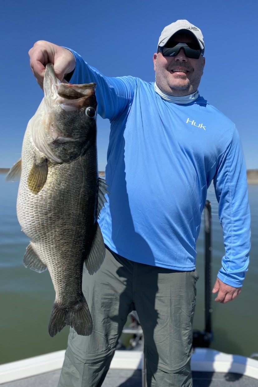 Man in blue Huk shirt holding massive bass on boat