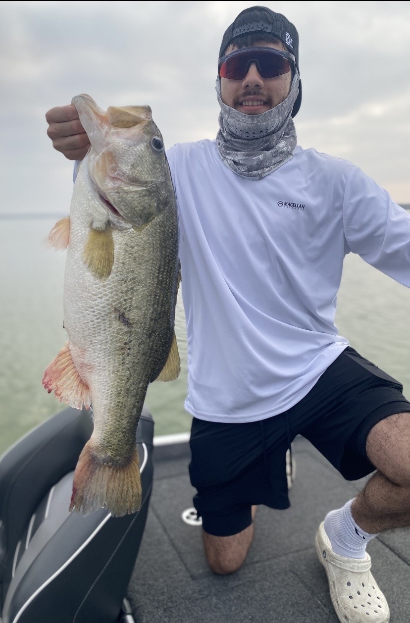 Angler in gaiter holding bass on boat