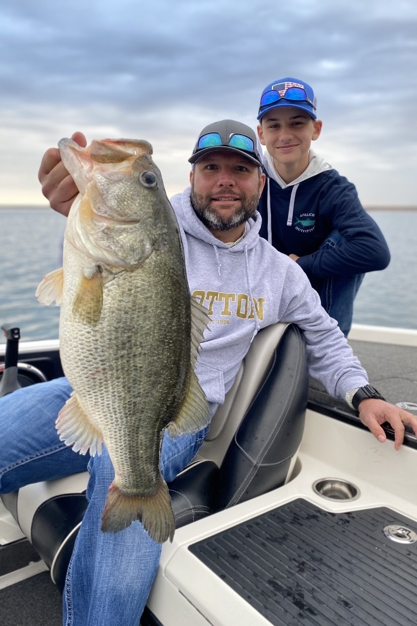 Man and teen on boat holding large bass on cloudy day