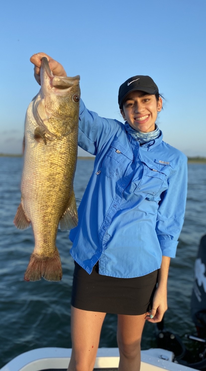 Young woman in blue Columbia shirt holding bass at sunset