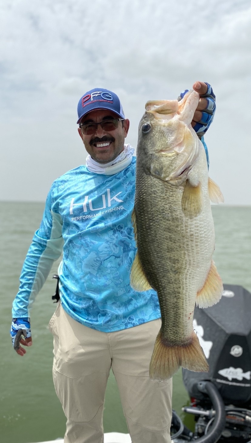 Man in Huk shirt holding massive bass on cloudy day