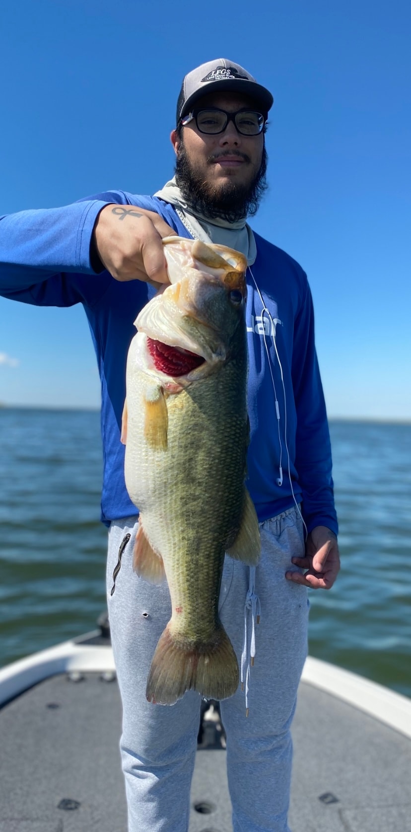 Man in blue LFGS cap holding bass on sunny day