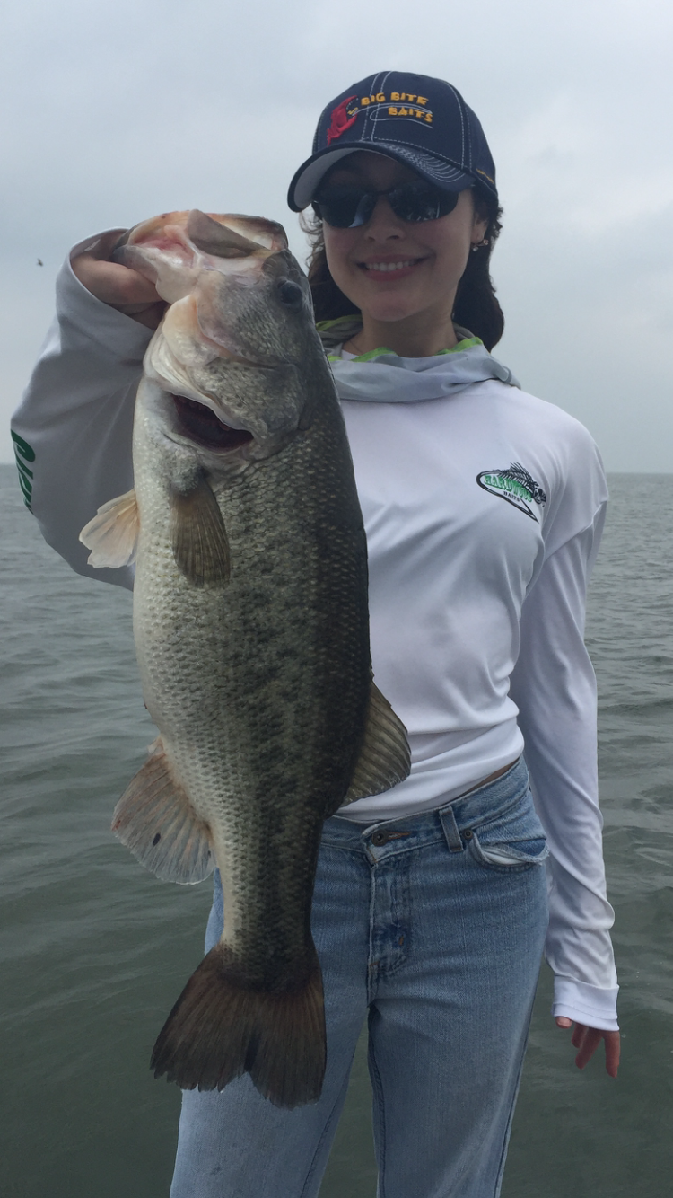 Woman in Big Bite Baits cap holding massive bass on cloudy day