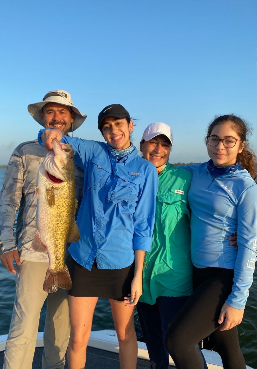 Family of four on boat holding large bass at sunset