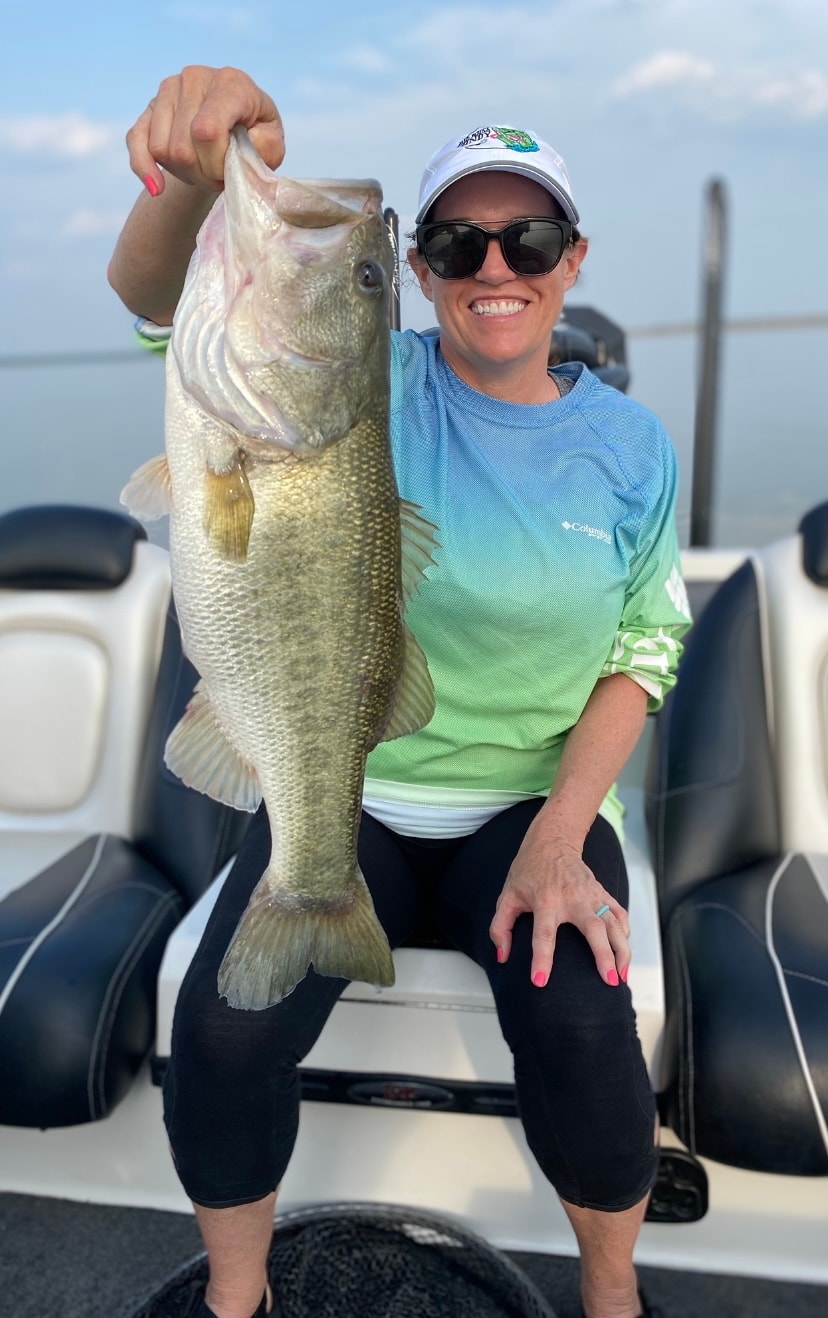Woman in Columbia shirt holding large bass on sunny day