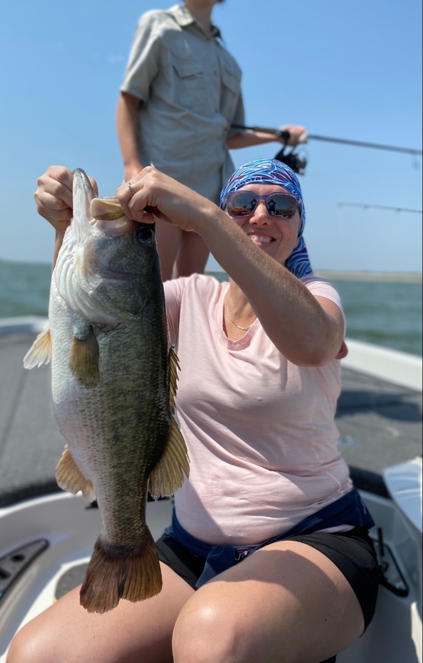 Woman in pink shirt and blue bandana holding large bass on sunny day