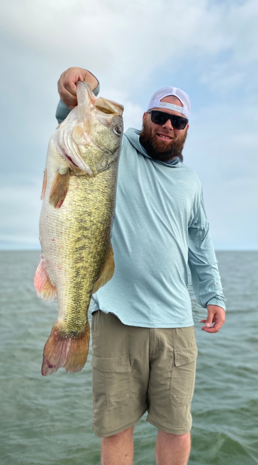 Man in light blue shirt holding massive bass on cloudy day