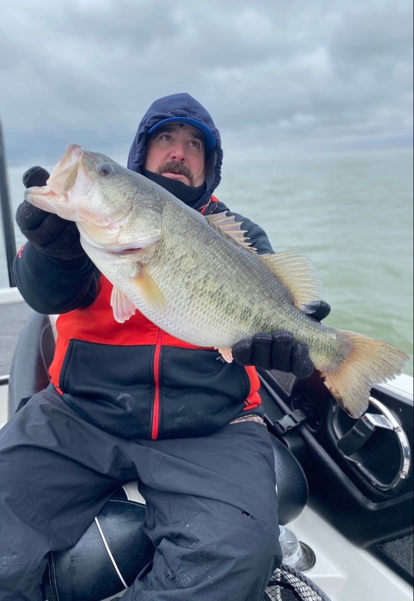 Man in blue rain gear holding massive bass on stormy day