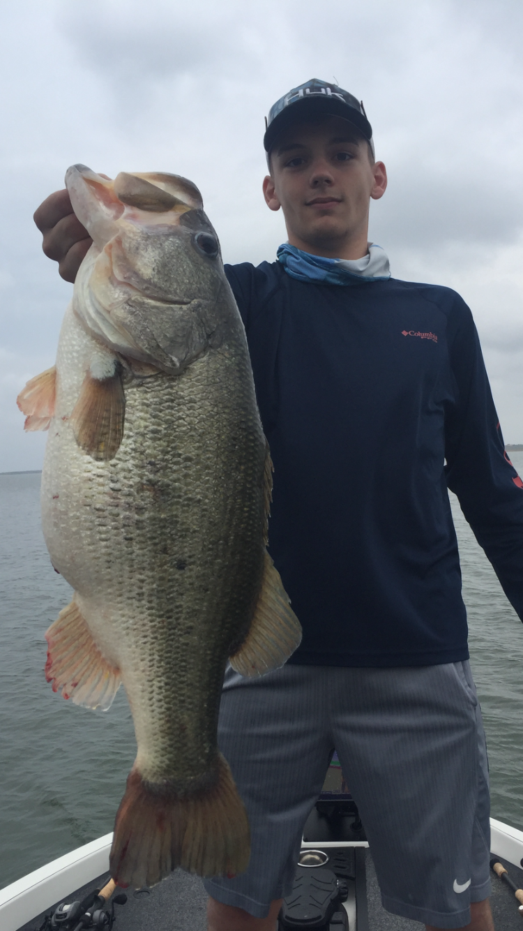 Teen in Huk cap holding large bass on cloudy day