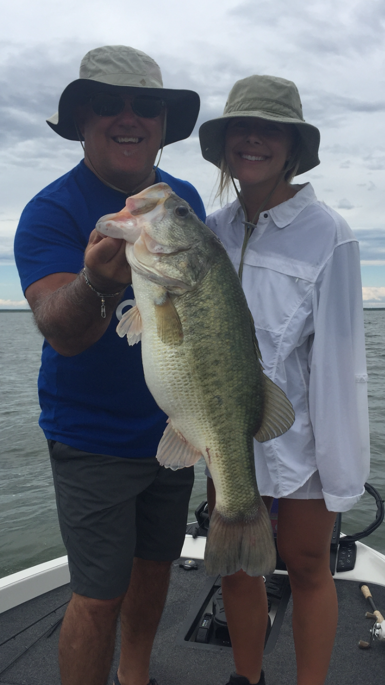 Man and girl in sun hats holding large bass on cloudy day