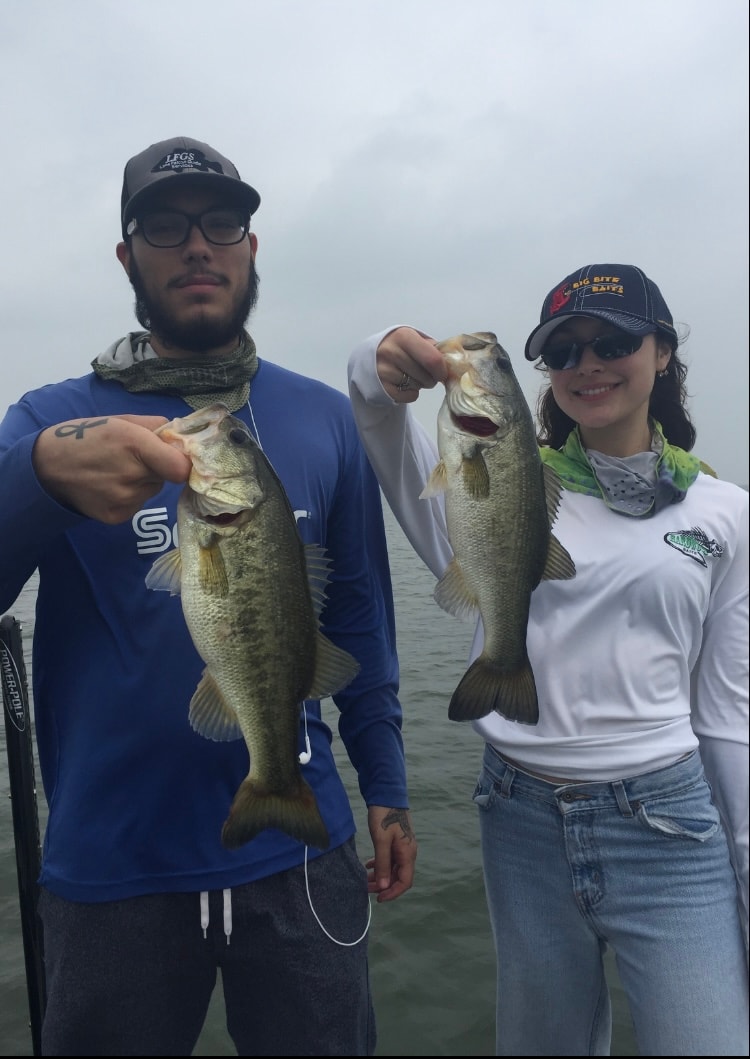 Man and woman in LFGS and Big Bite Baits caps each holding bass on cloudy day