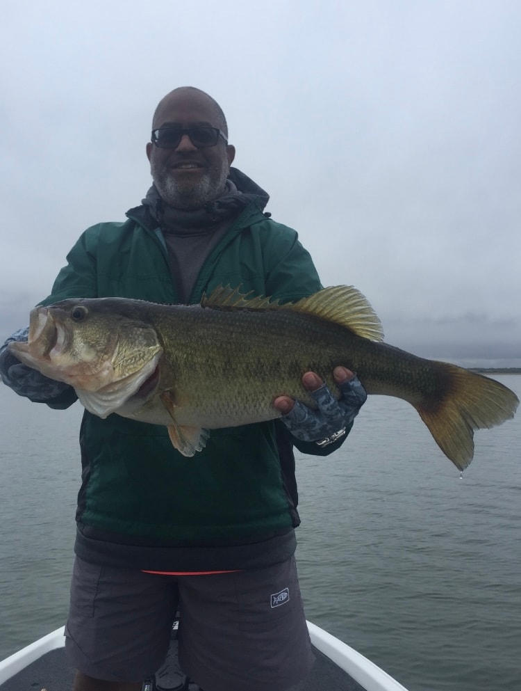 Man in green jacket holding massive bass on cloudy day