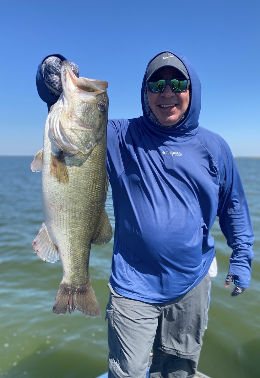 Man in Columbia hoodie holding large bass on sunny day